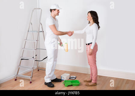 Young Beautiful Woman Shaking Hands To Painter With Paint Roller At Home Stock Photo