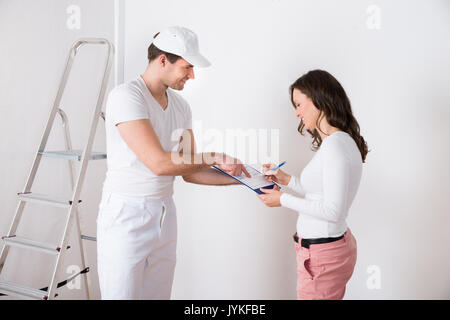 Young Woman Signing Document In Front Of Male Painter At Home Stock Photo