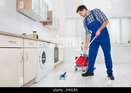 Young Male Worker Mopping Floor In Kitchen At Home Stock Photo