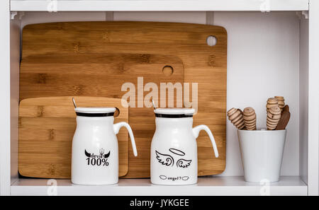 Big white mugs with spoons and Angel, Devil design on white shelf Stock Photo