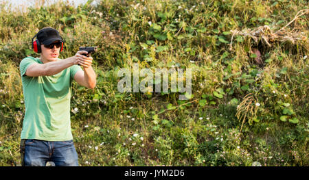 Young and handsome professional policeman special force trained battleground officer shooting with gun glock pistol at the enemy target in the wildern Stock Photo