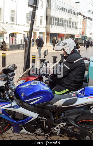 Motorbike courier sitting on a motorcycle with his helmet on resting with other parked machines Stock Photo