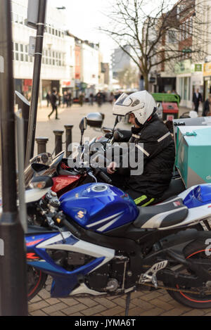 Motorbike courier sitting on a motorcycle with his helmet on resting with other parked machines Stock Photo