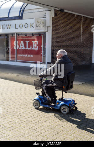 Elderly old man sits and rides on a mobility Scooter in a shopping area in Witham Essex England Stock Photo