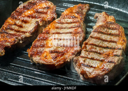 Raw Ribeye Steak with Herbs and Spices, frying on grill pan. Stock Photo