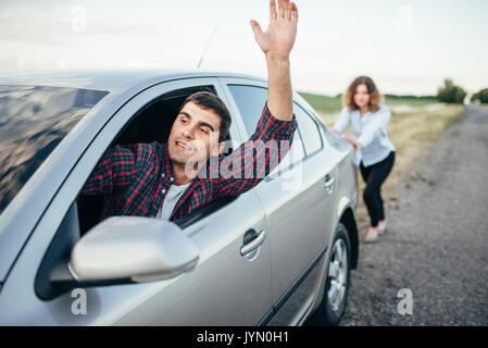 Woman pushing a broken car down the road, smiling man driver. Vehicle with trouble Stock Photo