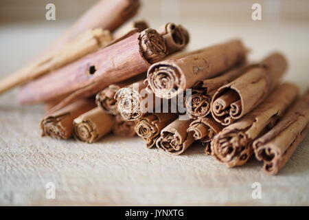 Dried, rolled true cinnamon (Cinnamomum verum) sticks in a pile on a wooden cutting board. Stock Photo