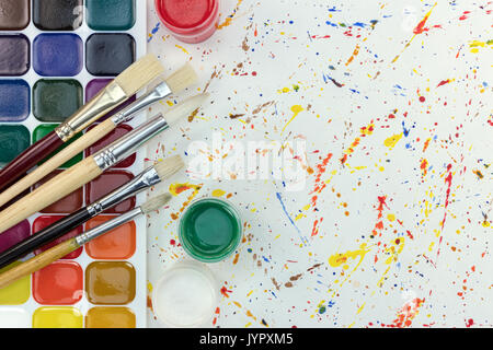 palette of watercolor paints, gouache buckets and brushes different size on colorful paint blobs background Stock Photo