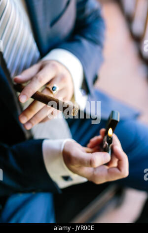 wedding, elegance, high fashion concept. tough arms of man, dressed in dark blue costume for celebration with snowy white cuffs, lightening big expensive cheroot Stock Photo