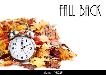 Alarm clock in colorful autumn leaves isolated against a white background with light shadow and shallow depth of field. Daylight savings time concept. Stock Photo