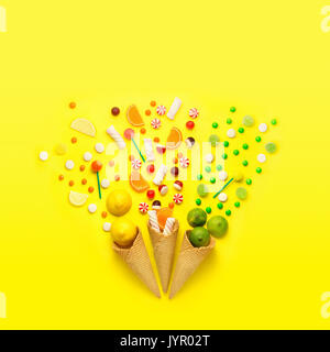 Creative still life photo of three waffle cones with candies, fruits and marshmallow on jellow background.