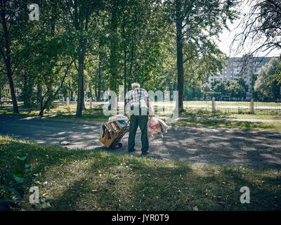 An elderly man collects garbage and waste paper. He is very badly dressed, he pulls a cart with mountains of papers and cardboard. Stock Photo