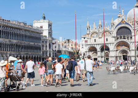 Tour group with families and children in Piazza San Marco, Venice, Italy following their tour guide carrying the blue umbrella walking towards the Bas Stock Photo