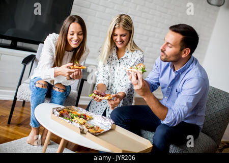 Small group of young friends eating pizza in the room Stock Photo