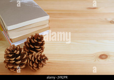 Three natural pine cones and stack of books on light brown wooden table, with free space for text and design Stock Photo