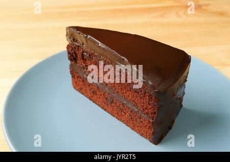 Piece of Delectable Chocolate Layer Cake Served on Blue Plate on the Wooden Table Stock Photo
