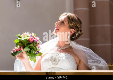 Bride at wedding in church with flower bouquet Stock Photo