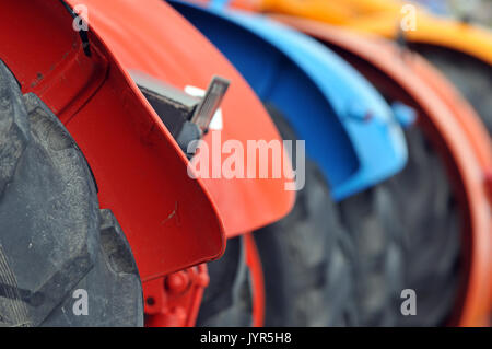 a line or row of brightly coloured painted vintage tractors showing big tyres and mudguards for ploughing and working the land large rubber tyres Stock Photo