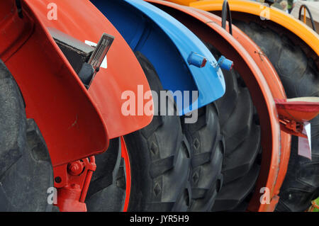 a line or row of brightly coloured painted vintage tractors showing big tyres and mudguards for ploughing and working the land large rubber tyres Stock Photo