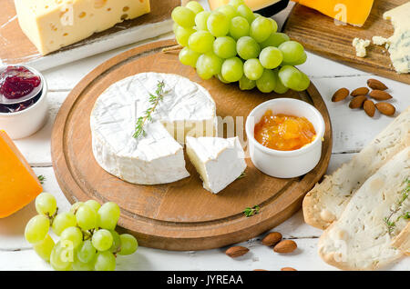 Different kinds of cheeses  with grapes, nuts  and jam on a white wooden board. Stock Photo