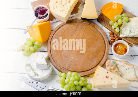 Assorted cheeses served with grapes, jam,  bread and nuts on a wooden background. Stock Photo