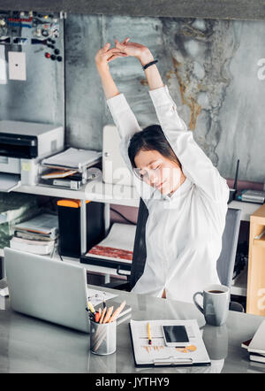 Asian businesswoman raise arm up stretching in front of desk from work on notebook screen in office,Office lifestyle concept. Stock Photo