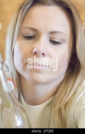 Young adult blonde woman looking at vintage water bottle. Close up candid portrait. Vertical crop Stock Photo