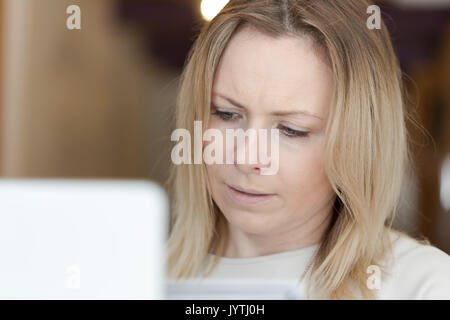 Young adult concerned woman working on laptop. Close up portrait, focus on head behind screen. Vertical composition Stock Photo