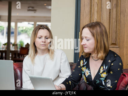 Two young businesswomen sitting on leather sofa having informal business meeting. Low angle pespective with selective focus on explicit face. Horizont Stock Photo