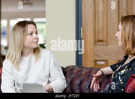 Two young businesswomen sitting on leather sofa having informal business meeting. Low angle perspective with selective focus on explicit face. Horizon Stock Photo