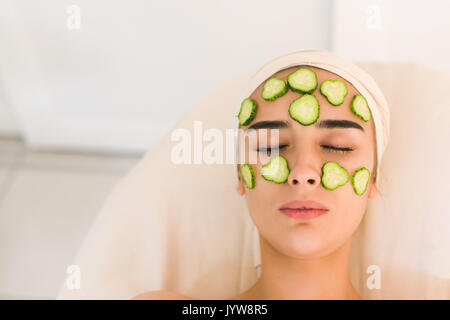 Cucumber slices on eyes. Young woman with facial mask of cucumber in beauty salon. Girl with closed eyes with a mask of cucumbers on her face. Stock Photo