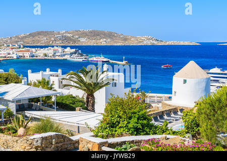 View of Mykonos sea bay with palm tree and windmill in foreground, Mykonos island, Greece Stock Photo