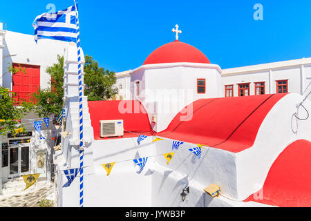 MYKONOS ISLAND, GREECE - MAY 17, 2016: Church building with red roof and Greek flag on whitewashed street in beautiful Mykonos town, Cyclades islands, Stock Photo