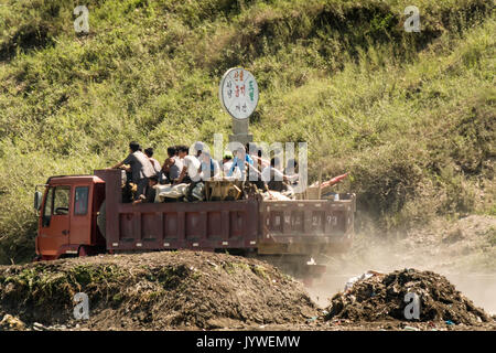 Hyesan, Ryanggang province, North Korea – August 7, 2017: People standing on an open truck driving on a dusty road. Stock Photo