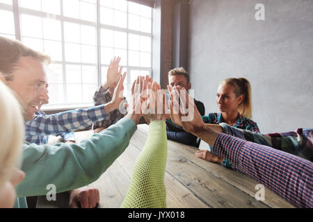 Modern business meeting concept, people in casual clothes sitting around wooden table giving high five Stock Photo
