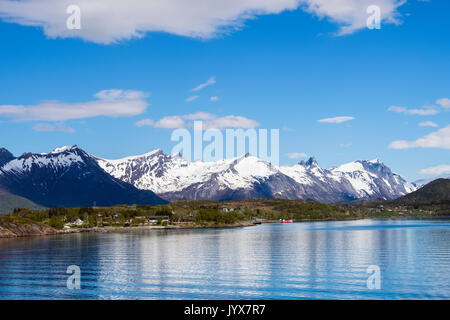 Offshore view to snowcapped mountains and campsite beside Arhaugfjorden fjord on Norwegian north west coast in summer. Furoy, Meløy, Nordland, Norway Stock Photo
