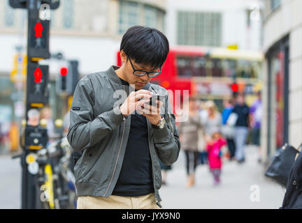 Young Japanese man in a UK city checking his smartphone while out. Stock Photo