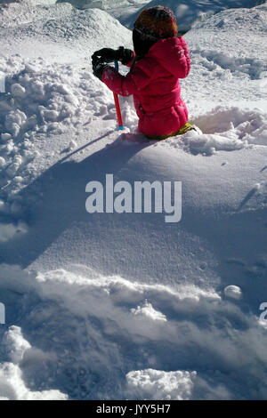 Young child stands in waist deep snow, looking out, holding a shovel Stock Photo