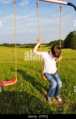 Sad lonely boy sitting on swing Stock Photo