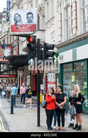 A group of women tourists waiting to cross the road outside the Apollo Theatre Shaftesbury Ave, Soho, London W1D 7EZ, UK