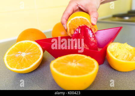 Halved oranges ready for being freshly squeezed in a red plastic juicer Stock Photo