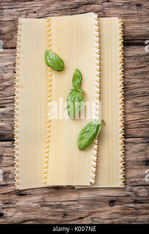 Preparing Italian lasagne with basil on wooden background Stock Photo