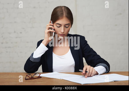 Business woman talking on phone and reading documents sitting at the table in office Stock Photo