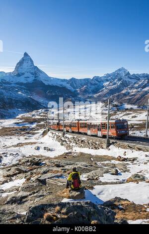 Hiker admires Matterhorn while white train of Gornergrat rides in the background. Zermatt, Canton of Valais, Switzerland Europe Stock Photo