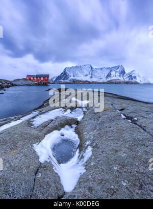 Typical red houses in the Hamnøy landscape with its cold sea and  snow capped peaks. Lofoten Islands Norway Europe Stock Photo