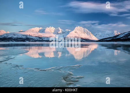 Blue sky and snowy peaks are reflected in the frozen Lake Jaegervatnet Stortind Lyngen Alps Tromsø Lapland Norway Europe Stock Photo