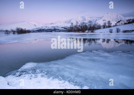 Snowy peaks are reflected in the frozen Lake Jaegervatnet at sunset Stortind Lyngen Alps Tromsø Lapland Norway Europe Stock Photo