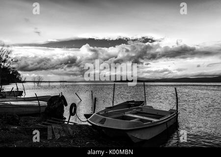 Some small fishing boat on a lake, beneath a cloudy, moody sky Stock Photo