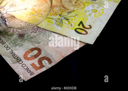 Two Brazilian Real money notes, of 50 and 20 value, currency of Brazil, on a black background and a lit light bulb on top, as a money idea and concept Stock Photo