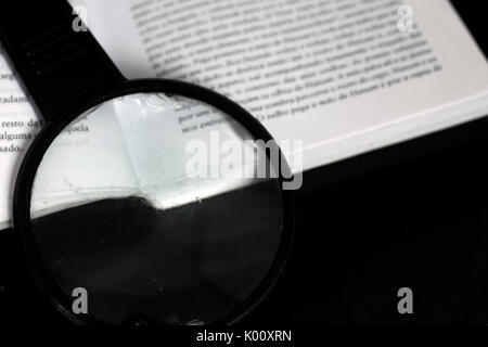 Magnifying glass on top of an open book on top of a black reflective glass surface Stock Photo